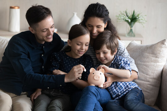 Happy family saving money for future purchase, making reserve fund, planning budget. Couple of parents and two little kids collecting cash, dropping coins into piggybank at home. Financial education