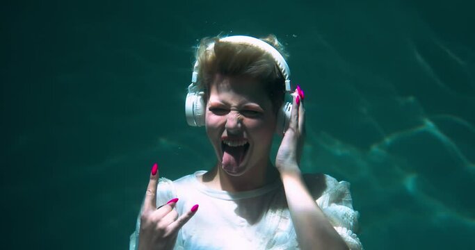 Cinematic under water shot, happy young female heavy metal fan dancing to loud rock music in headphones slow motion.