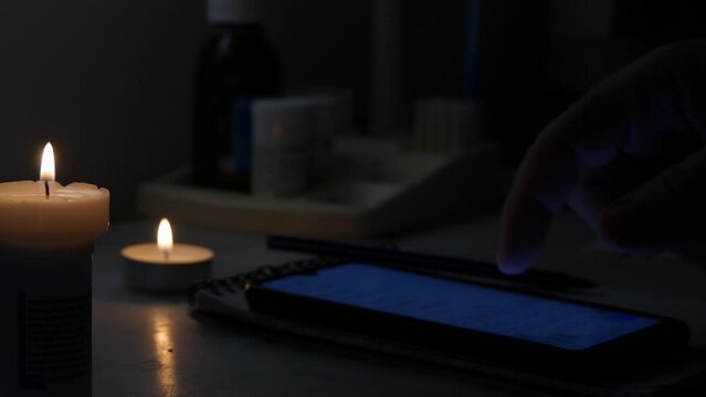 Man Using a Cellphone, in a Dark Room Illuminated with a Lighted Candle in Time of an Accidental Power Failure.
