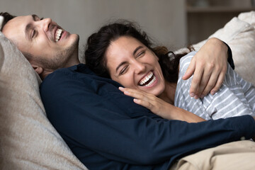 Joyful millennial couple having fun and enjoying closeness at home, hugging on couch, relaxing,...