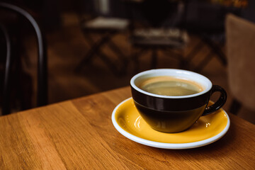 A ceramic cup of black coffee on the wooden table in a cafe.
