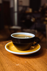 A ceramic cup of black coffee on the wooden table in a cafe.