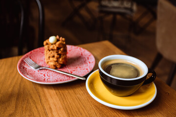 A ceramic cup of black coffee and a dessert served on a plate on the wooden table in a cafe.