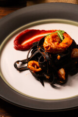 Squid-ink fettuccine with tomato sauce and shrimp in white dish serve with white wine.