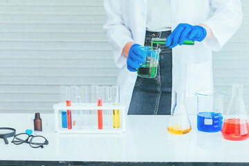 Fototapeta premium Hand of Scientist in uniform holding beaker and test tube have chemical liquid for testing chemical reaction.