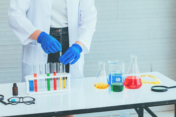 Hand of Scientist in uniform holding beaker and test tube have chemical liquid for testing chemical reaction.