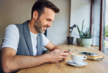 Mid adult man using smartphone while sitting at cafeteria during coffee break