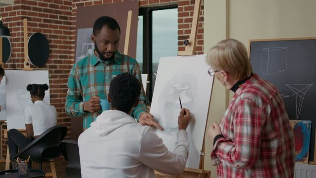 Old teacher and student helping african american man to draw vase on canvas. Diverse team of people explaining artisitc technique to develop drawing skills in art class, new years resolutions.