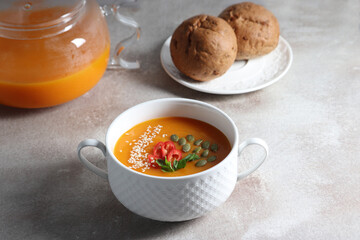 Vegetarian pumpkin soup with herbs in a bowl and homemade rye buns on a gray background