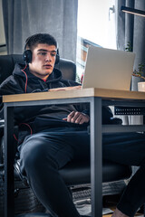 A young male athlete sits in front of a laptop in his room.