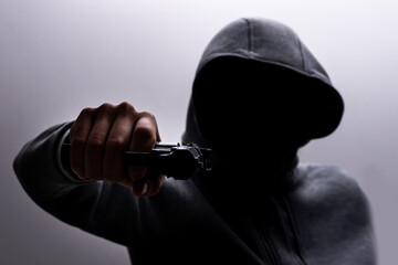 Photo of a creepy horror criminal in black hoodie holding revolver gun.