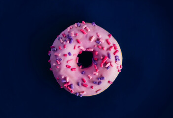 One pink sweet delicious donut with multicolored sprinkles lies on a dark blue background. Bakery...