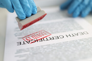 Pathologist putting red covid19 stamp on death certificate closeup