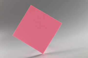 Pink square sticker standing on sharp edge on grey background