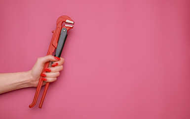 A plumbing wrench in a woman hand on a pink background. Copy-space in a right part of image.
