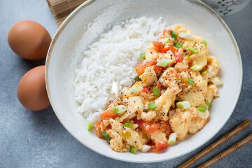 Beige plate with chinese tomato egg-stir fry and white rice, elevated view on a light-blue stone surface, middle close-up