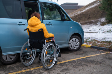 Caucasian woman in a wheelchair gets into the car. 