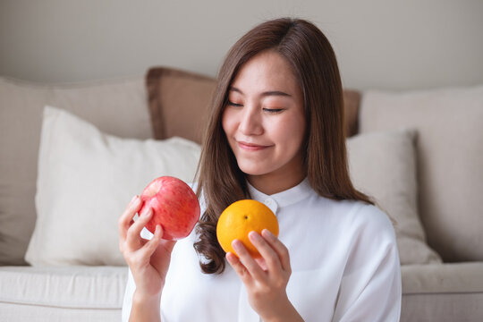 Portrait image of a beautiful young woman holding and showing an orange and a red apple