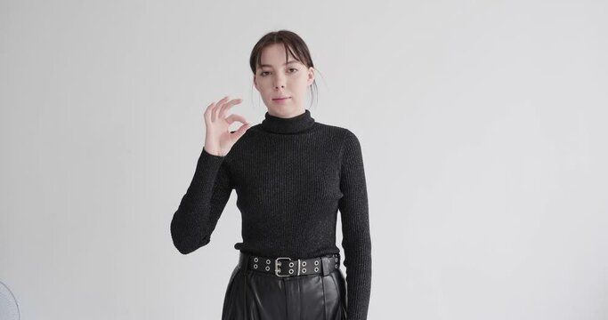 young girl in black clothes on white background waving her hands shows something using sign language of deaf and dumb 