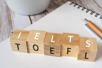 「IELTS」「TOEFL」と書かれた積み木、ペン、ノート、コーヒーカップ