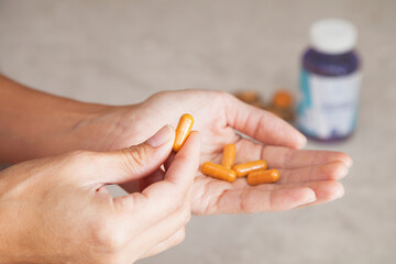 Woman's hand holding orange turmeric vitamin medicine supplement pill capsules with bottle in the background