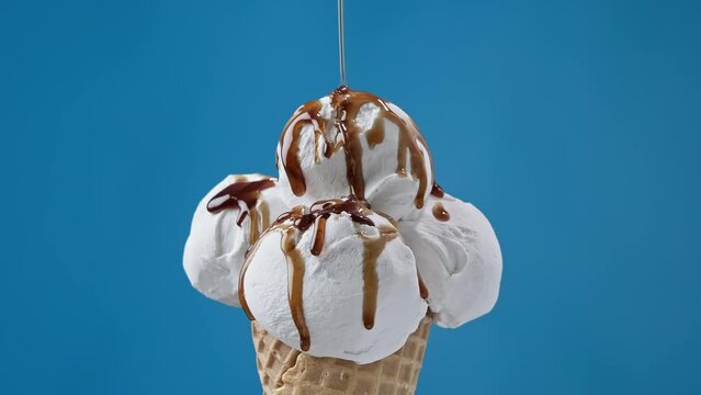 Caramel topping flowing on white ice cream at blue background. Ice cream in cone with caramel sauce. Food concept. Close-up in 4K, UHD