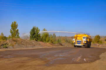 Fototapeta na wymiar Heavy truck pours the road with water in the iron ore quarry. Dust removal, protection of the environment. Irrigation of the road from dust.