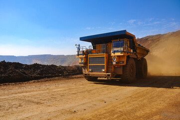 Mining dump truck transports rock, iron ore along the side of the quarry.