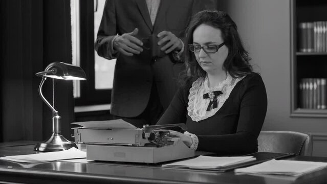 Male Dictating Text to Write to his Secretary, Female Using Retro Typewriter in the Office. Slow Motion. Film Noir (Monochrome Toning)