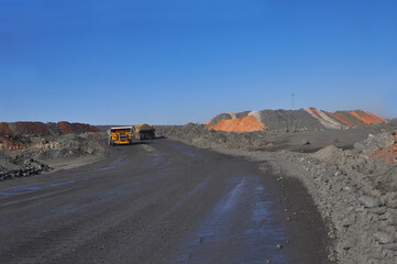 Mining dump truck transports rock, iron ore along the side of the quarry.