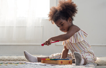 Cute little mixed race toddler girl playing with wooden toy xylophone.