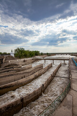 Fototapeta na wymiar Dam of Shardara river. Concrete elements of Shirkeily channel. Yellow water. Blue sky, clouds. Kyzylorda, Kazakhstan