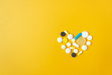 Top view of different tablets and capsules in the shape of heart on a yellow background. Health and medicine concept.
