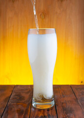 a thin trickle of light beer flows into a glass glass, beer with a thick rising white foam. wooden...