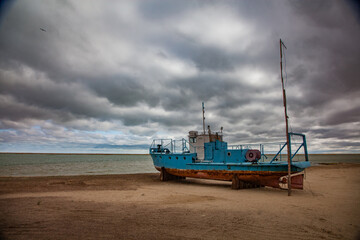 Fototapeta na wymiar Kok-aral, Kazakhstan - 03 May, 2012: Small Aral sea Kok-aral sand dam. Fishing boat on the beach. Aral on horizon. Grey stormy clouds.