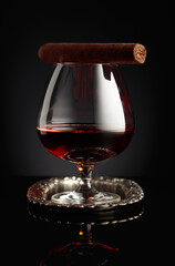Snifter of brandy and cigar on a black background.