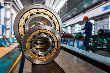 Two roll bearing close-up photo. First bearing in focus. Locomotive repair plant interior and worker on background, blurred. - obrazy, fototapety, plakaty