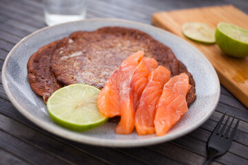 healthy breakfast of pieces of salted smoked salmon with buckwheat pancakes and lime