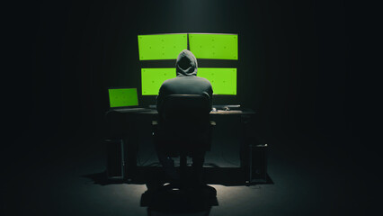 Concept shot of anonymous man in hoodie writing code to hack database while sitting at desk with...