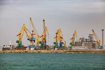 Aktau, Kazakhstan - May 19 2012: Cargo seaport loading terminal on Caspian sea. Yellow dock cargo cranes. Grain elevator right. Grey sky
