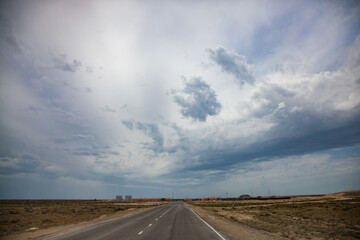 Fototapeta premium Desert road to Aktau seaport and loading terminal. Beautiful cloudy sky. Pre-storm weather.
