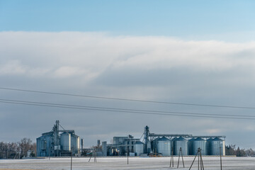 A large modern plant for the storage and processing of grain crops. view of the granary on a frosty sunny day. Silver silo grain storage in winter covered with snow