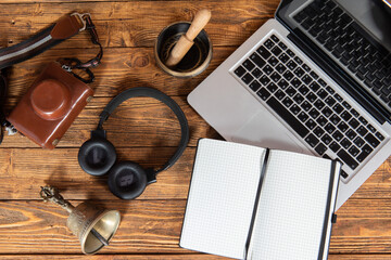 flatlay on a wooden background with a laptop headphones camera and a white notebook in a cage with a field for writing. empty space