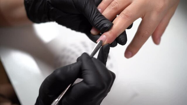 the hands of a professional salon worker holding a client's hand while using a cuticle pusher. Manicurist using cuticle pusher on girl's hands. Manicurist makes a manicure in a nail salon.