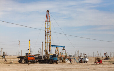 Fototapeta na wymiar Works on oil drill rig. Workers, auto, trucks and pumping jack in desert. Zhanaozen, Kazakhstan.