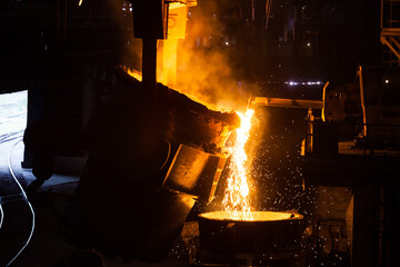 Molten metal pouring from metallurgy ladle. Smoke, on black background.