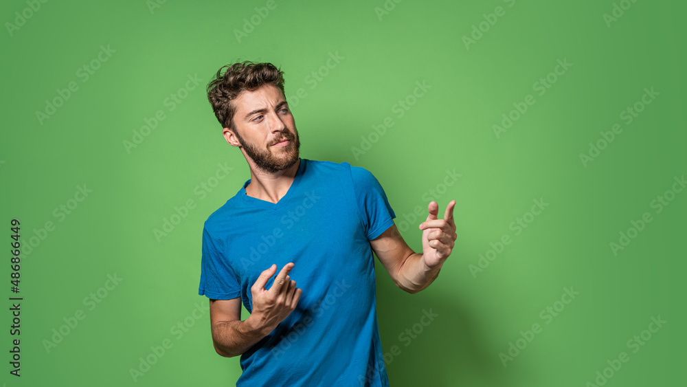 Wall mural Handsome young man isolated on green background pointing index fingers to an empty room for text or copy space