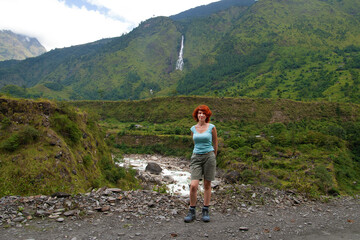 Young woman is posing against the backdrop of a beautiful view with waterfall, Annapurna trekking, Nepal