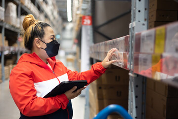 Fat woman worker inspecting stock of products while working in large warehouse. face mask during coronavirus and flu outbreak. Virus and illness protection