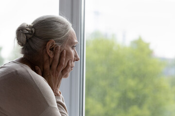 Upset lonely senior lady looking out of window with despair, frustration, going through depression,...